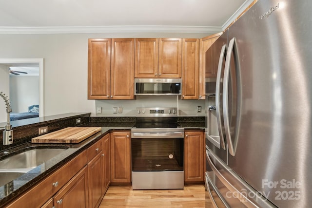 kitchen featuring stainless steel appliances, light wood finished floors, ornamental molding, and brown cabinets