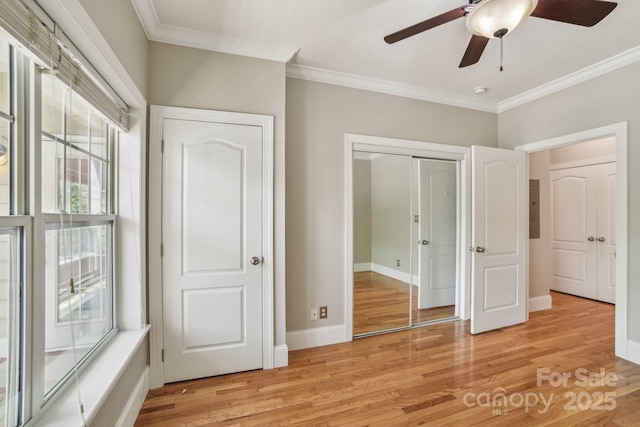 unfurnished bedroom with crown molding, light wood-style flooring, baseboards, and a closet