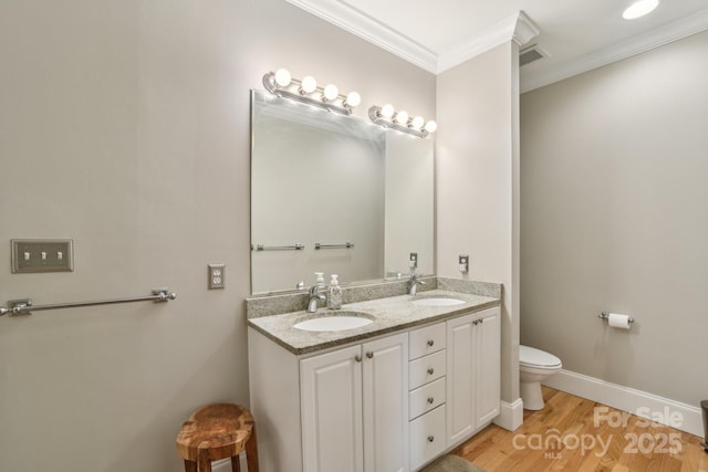 bathroom featuring ornamental molding, toilet, double vanity, wood finished floors, and baseboards