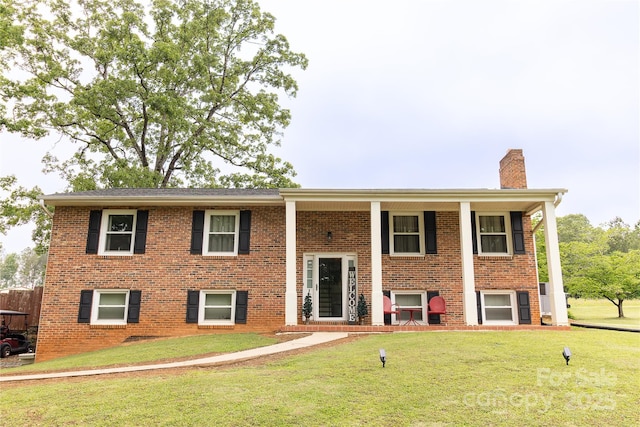 raised ranch featuring a chimney, brick siding, a front lawn, and a porch
