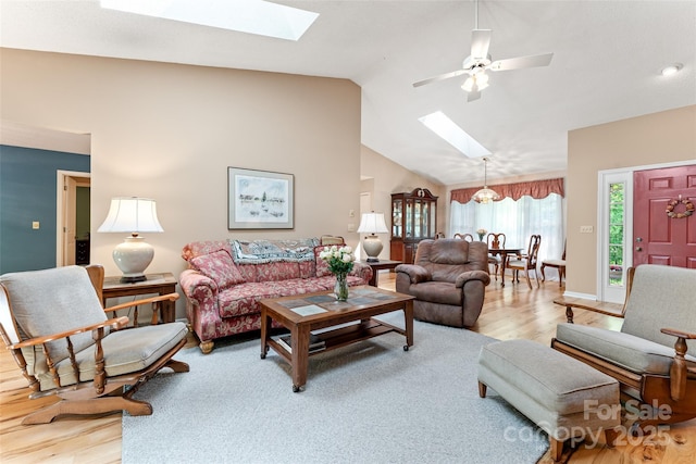 living area with a skylight, light wood-style floors, a ceiling fan, high vaulted ceiling, and baseboards