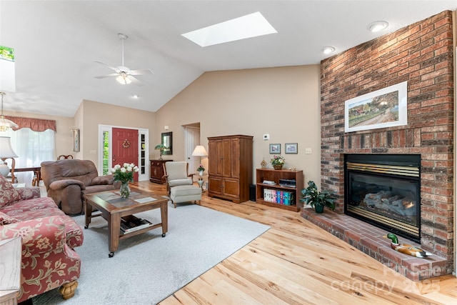 living area featuring wood finished floors, a fireplace, ceiling fan, a skylight, and high vaulted ceiling