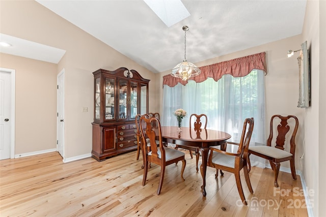 dining area featuring a skylight, a chandelier, light wood-type flooring, baseboards, and vaulted ceiling