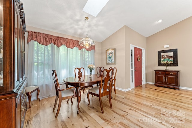 dining area featuring a skylight, light wood-type flooring, vaulted ceiling, a chandelier, and baseboards