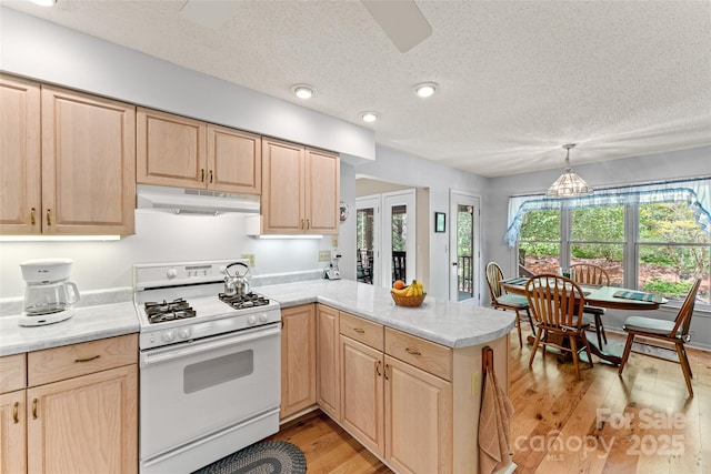 kitchen featuring white range with gas stovetop, light brown cabinets, under cabinet range hood, a peninsula, and a textured ceiling