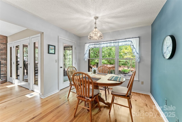 dining room featuring a chandelier, light wood-style floors, plenty of natural light, baseboards, and a textured ceiling