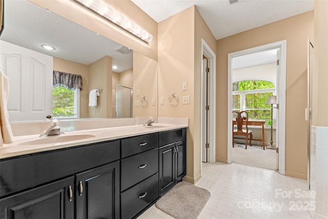 full bath featuring healthy amount of natural light, a shower stall, double vanity, baseboards, and a textured ceiling