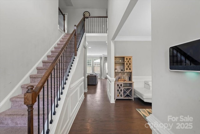 foyer entrance featuring stairs, ornamental molding, dark wood finished floors, a wainscoted wall, and a decorative wall