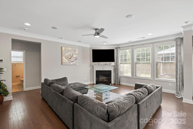 living area featuring a ceiling fan, a fireplace with flush hearth, baseboards, ornamental molding, and dark wood finished floors