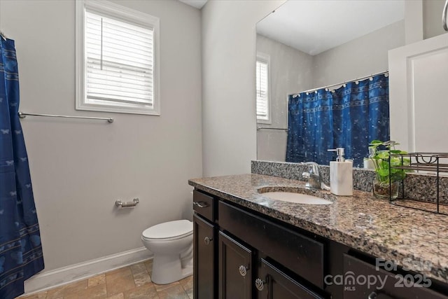 bathroom featuring baseboards, toilet, vanity, curtained shower, and stone finish floors