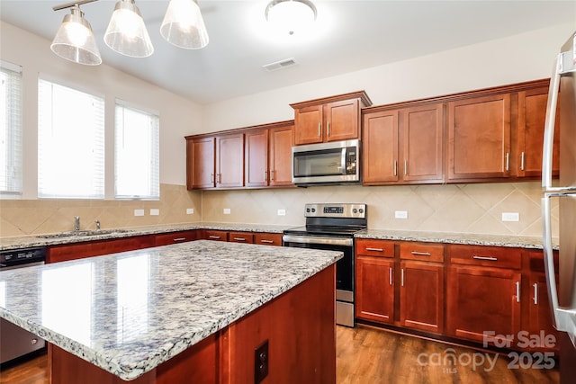 kitchen featuring stainless steel appliances, a sink, a center island, tasteful backsplash, and light stone countertops