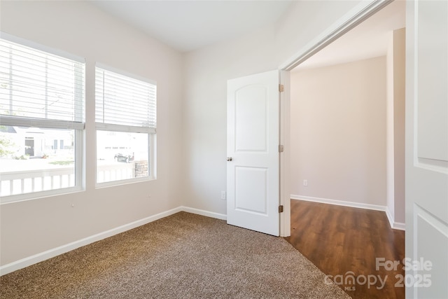 empty room featuring baseboards and dark colored carpet