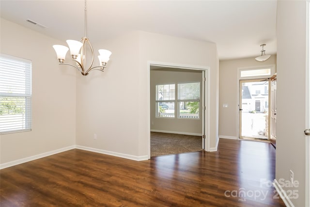 empty room featuring dark wood-style flooring, a chandelier, and baseboards