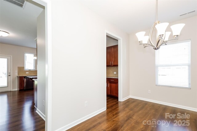 unfurnished dining area featuring a chandelier, dark wood finished floors, and baseboards