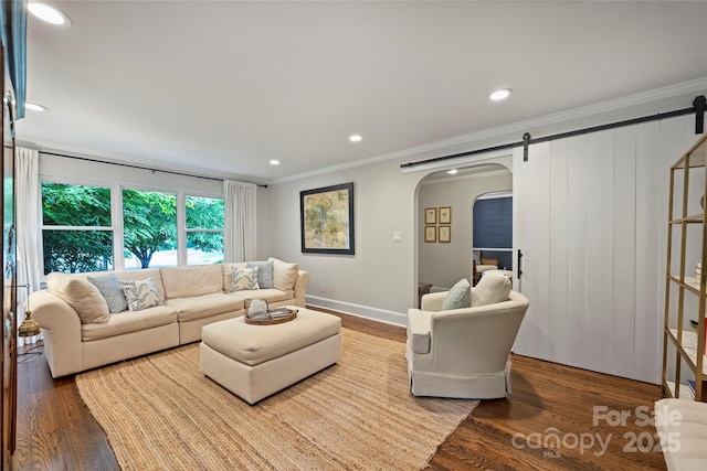 living area with a barn door, arched walkways, crown molding, wood finished floors, and recessed lighting