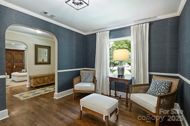 sitting room with arched walkways, wallpapered walls, crown molding, wood finished floors, and baseboards