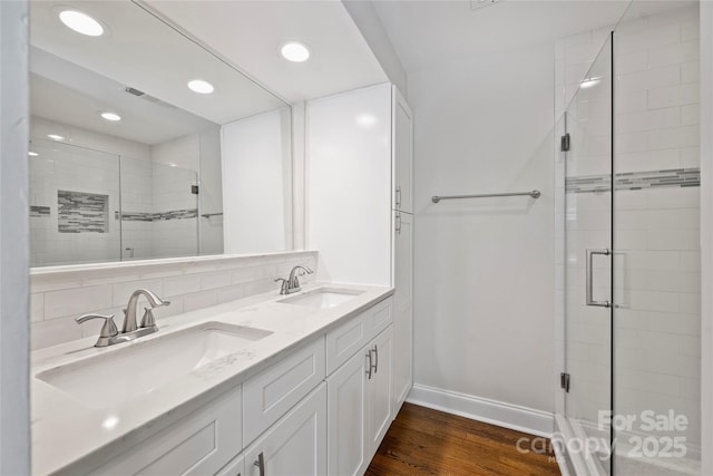 full bath featuring a shower stall, wood finished floors, baseboards, recessed lighting, and double vanity