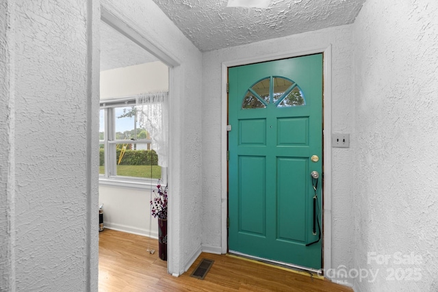 entrance foyer with a textured wall, wood finished floors, baseboards, and a textured ceiling