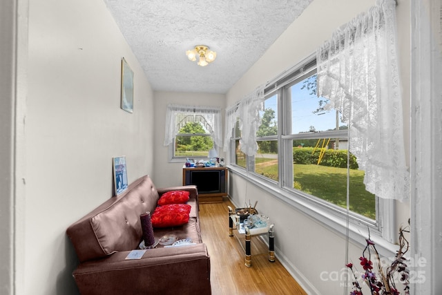 sunroom with wood finished floors, a textured ceiling, and baseboards
