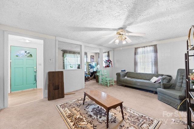 living room with light carpet, a ceiling fan, and a textured ceiling