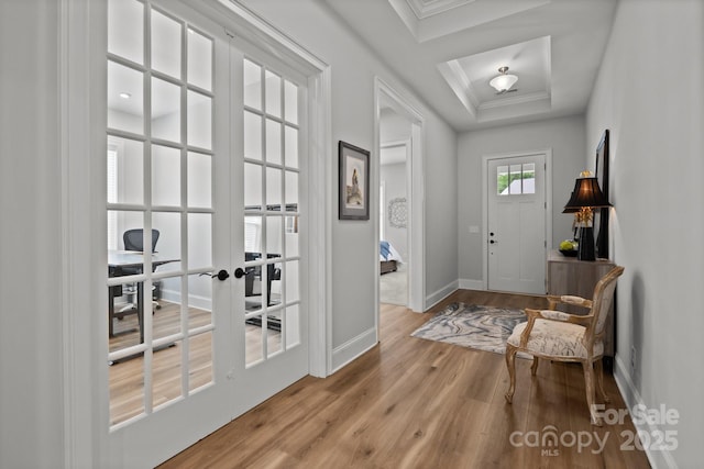 entrance foyer with wood finished floors, a raised ceiling, baseboards, crown molding, and french doors