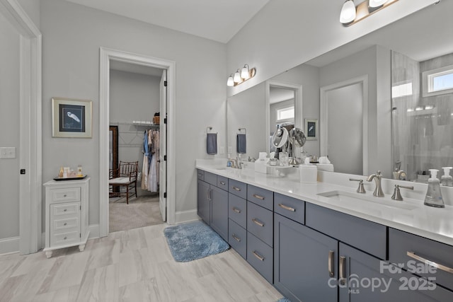 full bathroom featuring double vanity, a spacious closet, walk in shower, and baseboards