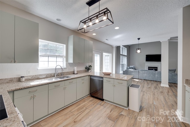 kitchen with stainless steel dishwasher, a textured ceiling, a sink, light wood-style floors, and a peninsula