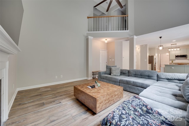 living room featuring light wood-style floors, high vaulted ceiling, baseboards, and a fireplace
