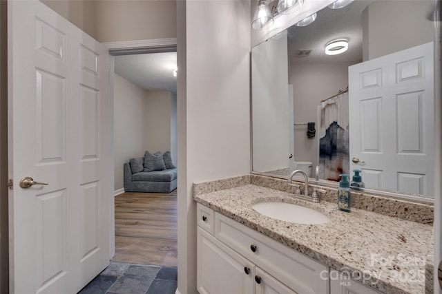 full bathroom featuring vanity, a textured ceiling, a shower with shower curtain, and stone finish flooring