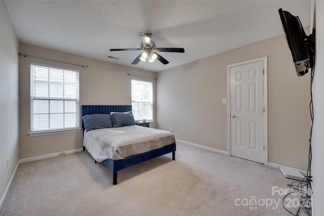 bedroom with light colored carpet, a textured ceiling, baseboards, and a ceiling fan