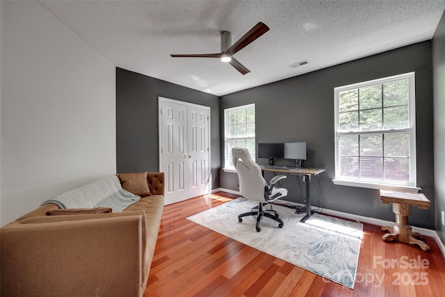 office featuring plenty of natural light, a ceiling fan, a textured ceiling, wood finished floors, and baseboards