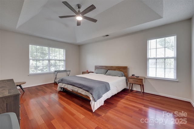 bedroom with a raised ceiling, multiple windows, wood finished floors, and baseboards