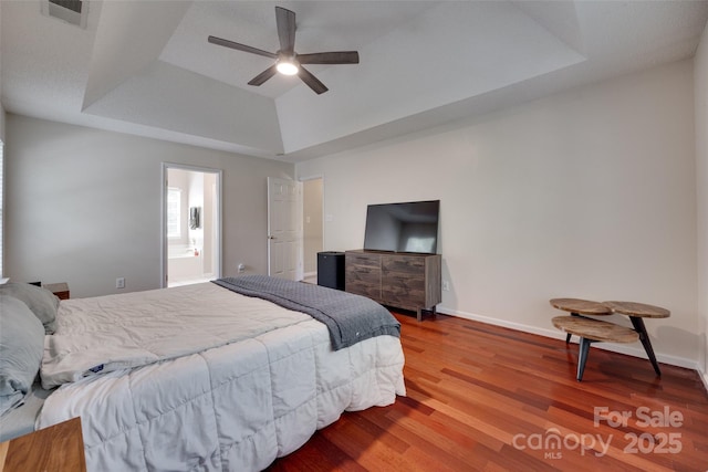 bedroom featuring a tray ceiling, wood finished floors, baseboards, and ceiling fan