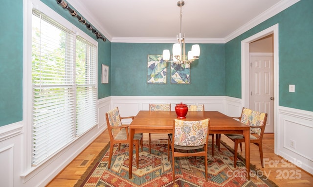 dining area with a chandelier, a wainscoted wall, light wood-style floors, a decorative wall, and ornamental molding