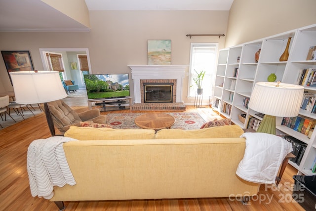 living area featuring a brick fireplace, wood finished floors, and crown molding