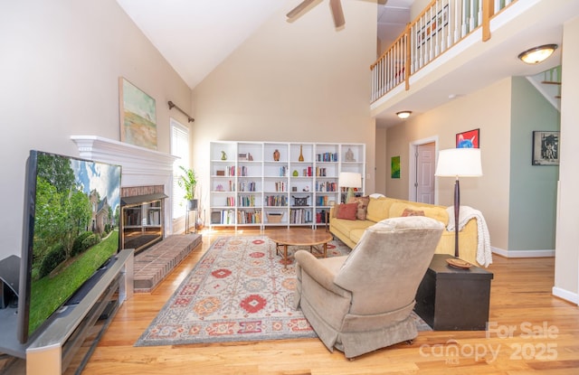 living room with wood finished floors, a brick fireplace, baseboards, ceiling fan, and high vaulted ceiling