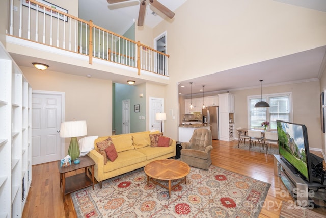 living area featuring light wood-type flooring, a ceiling fan, crown molding, and a high ceiling