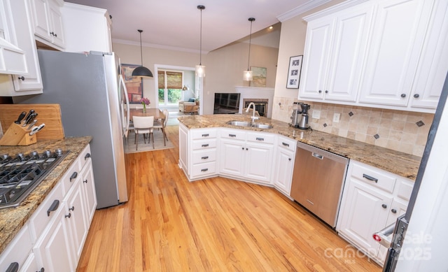 kitchen with appliances with stainless steel finishes, a sink, light wood finished floors, a peninsula, and crown molding