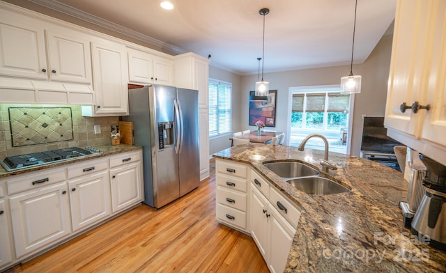 kitchen featuring stainless steel appliances, a sink, light wood-style flooring, ornamental molding, and white cabinets