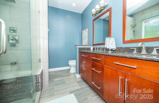 full bathroom featuring toilet, a shower stall, baseboards, and double vanity