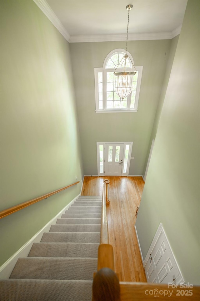 stairway with a chandelier, wood finished floors, crown molding, and baseboards