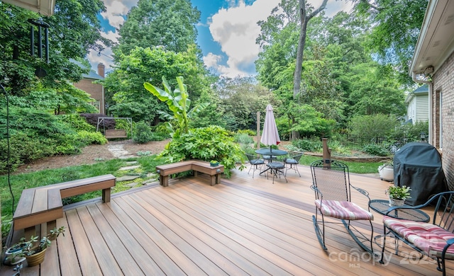 deck featuring outdoor dining space, fence, area for grilling, and view of wooded area