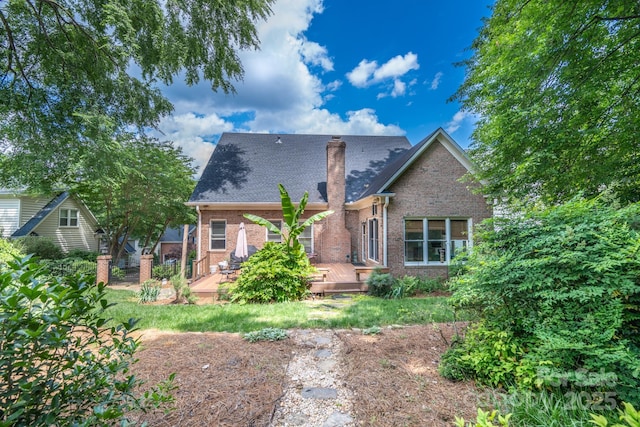 back of property with brick siding, a chimney, a wooden deck, and roof with shingles