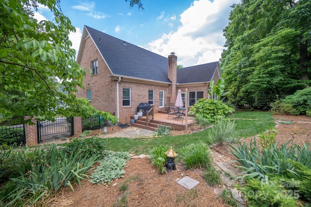 rear view of property featuring a deck, brick siding, fence, a chimney, and roof with shingles