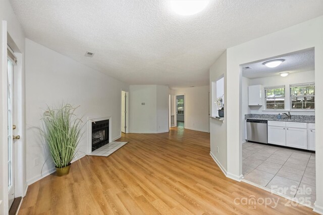 6016 Gray Gate Ln Unit C, Charlotte, NC 28210 - unfurnished living room with a textured ceiling, light wood finished floors, a fireplace with flush hearth, a sink, and baseboards