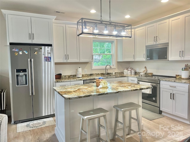 kitchen with appliances with stainless steel finishes, light wood finished floors, a kitchen island, a sink, and light stone counters