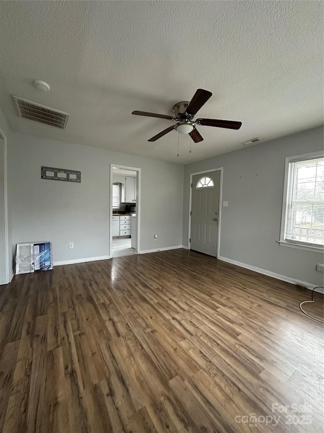 unfurnished living room with dark wood-style floors, a textured ceiling, ceiling fan, and baseboards