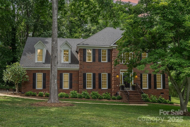 colonial house featuring a front yard, brick siding, and a shingled roof