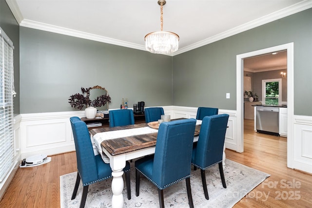dining space with a chandelier, ornamental molding, light wood-style floors, wainscoting, and a decorative wall