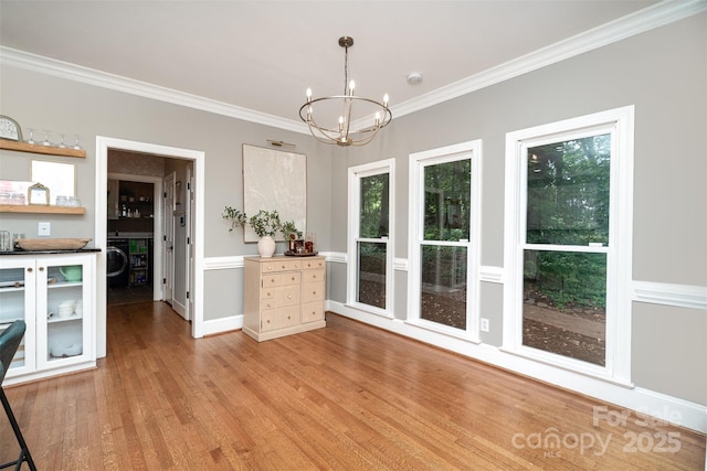 dining room with crown molding, a chandelier, light wood-style flooring, washer / dryer, and baseboards